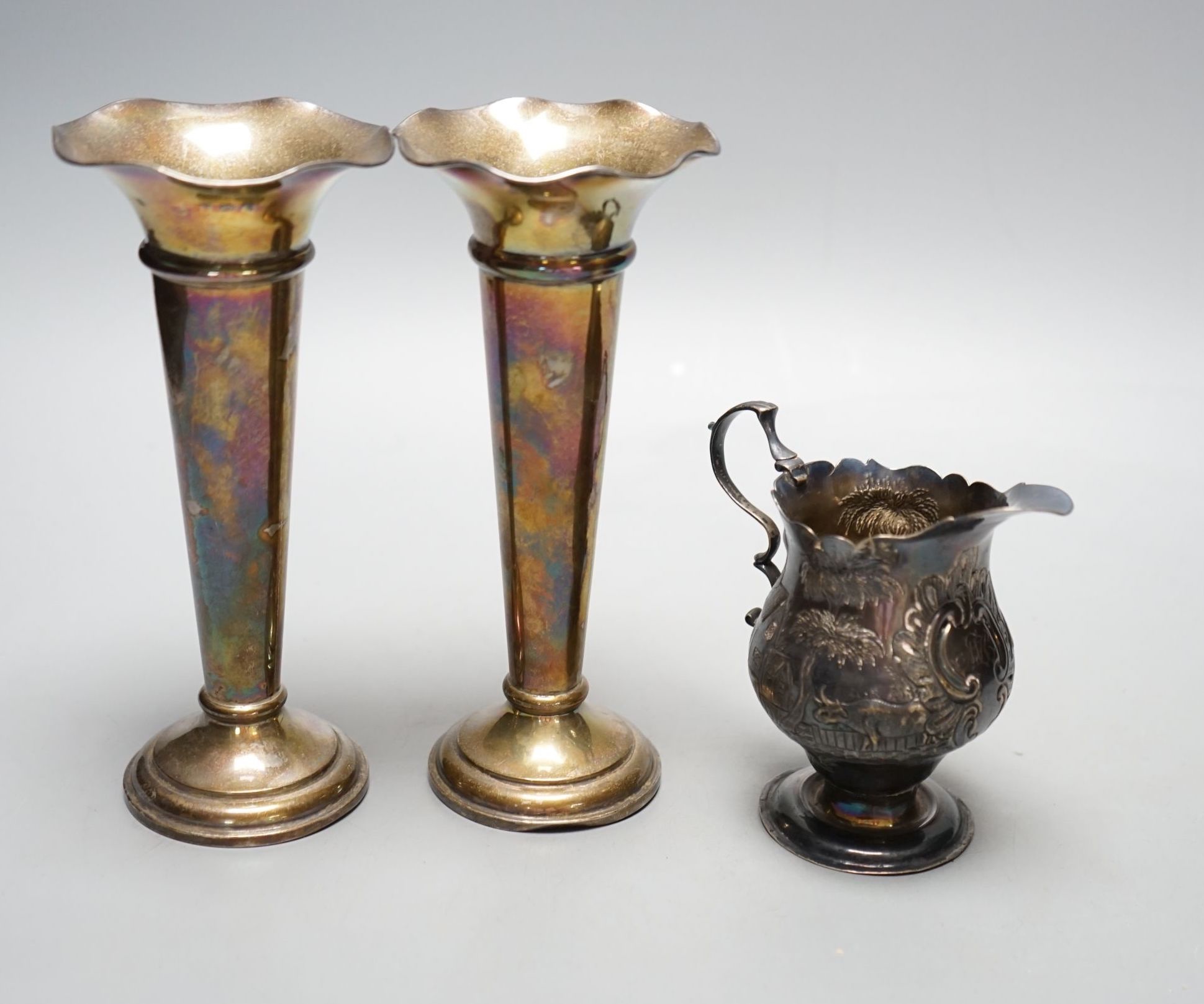 A George III silver helmet shaped cream jug, with later embossed decoration, London, 1759, 97mm and a pair of Edwardian silver spill vases, 16.3cm.